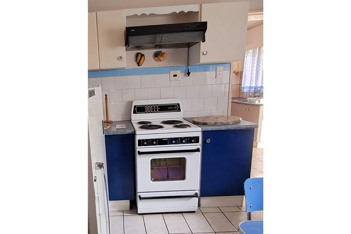 A dated kitchen featuring blue and cream cabinetry, a freestanding electric stove with extractor fan, and tiled splashbacks.