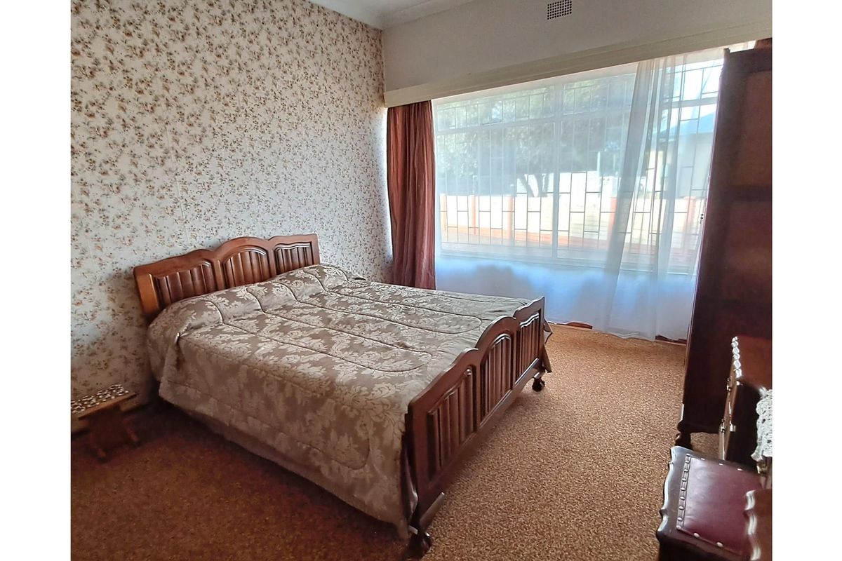 A bedroom featuring large windows with security bars, patterned wallpaper, and carpeted flooring.