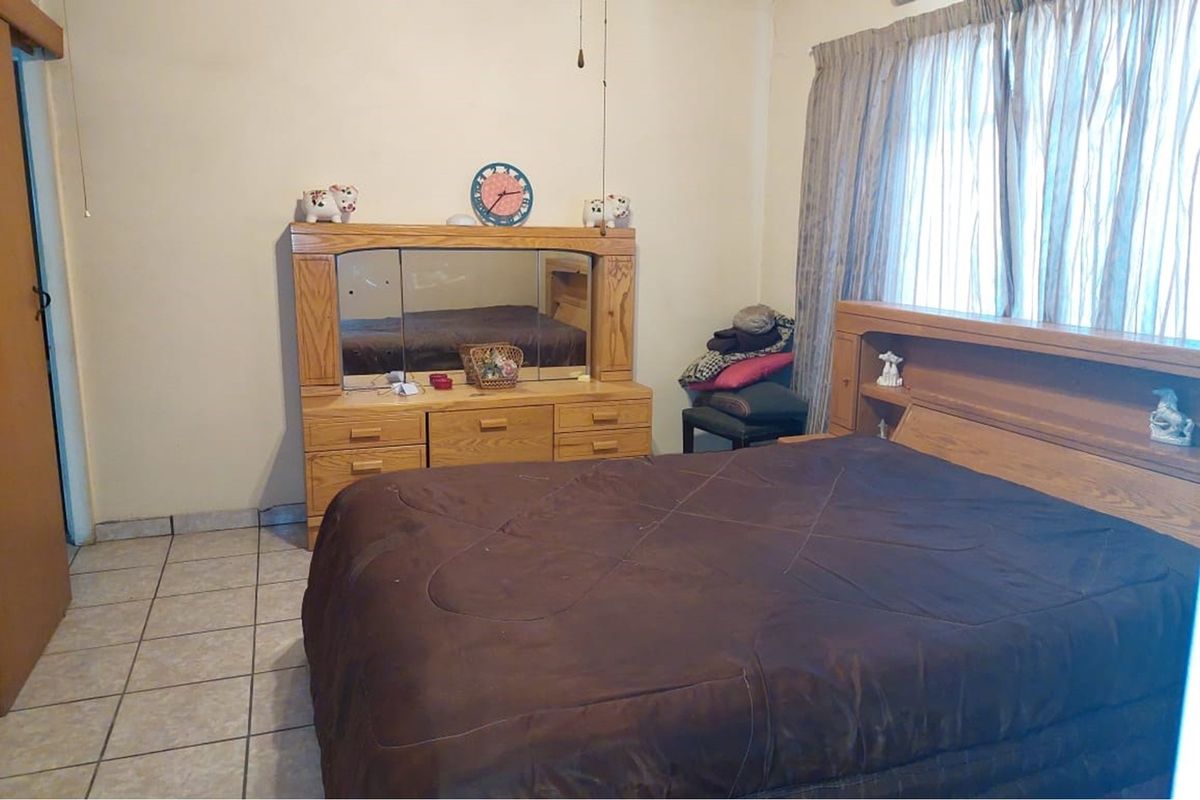 A bedroom featuring tiled flooring and a built-in headboard unit, offering a functional space with neutral wall finishes.