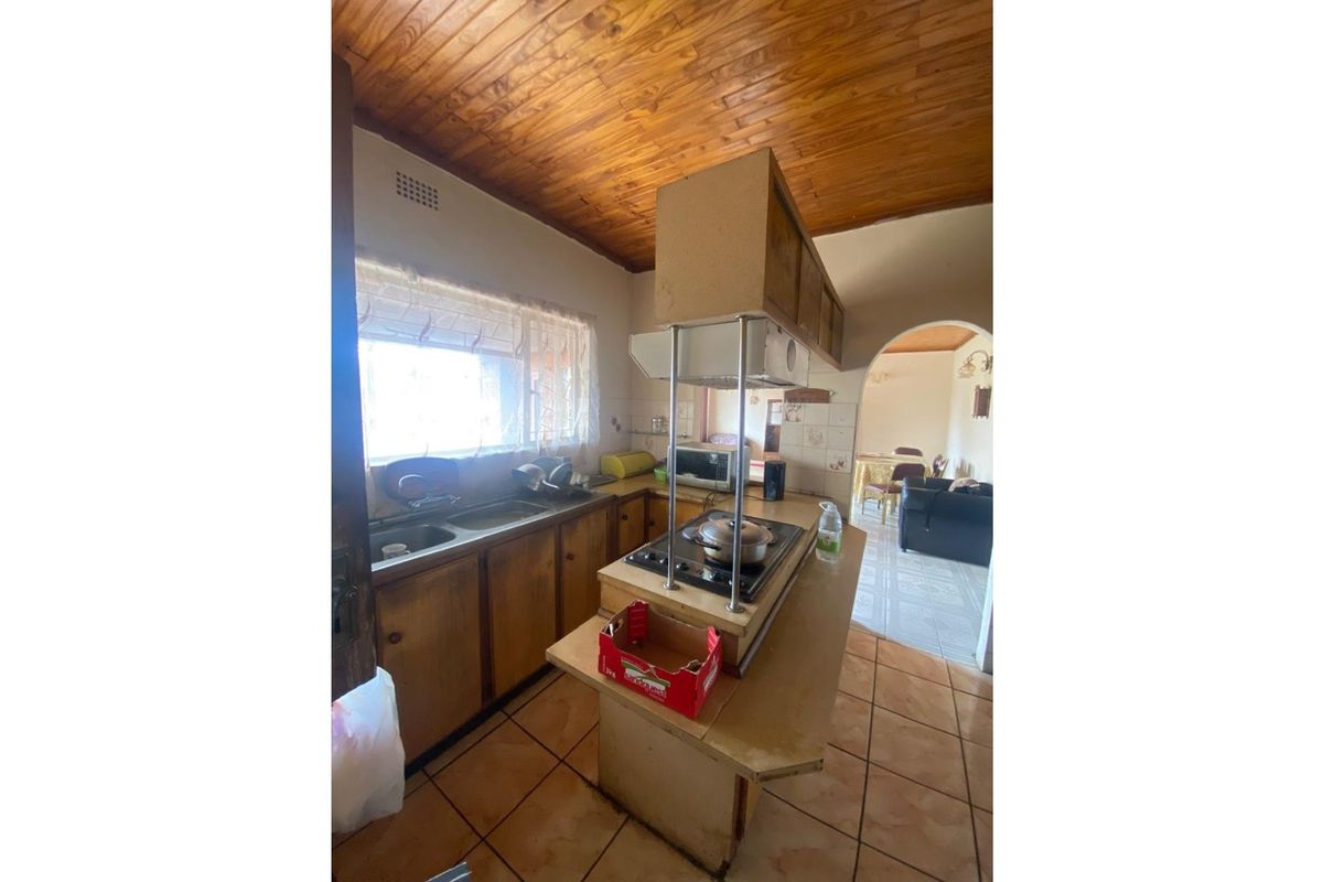 A dated kitchen featuring wooden cabinetry, a central island with a built-in hob, and a distinctive timber-paneled ceiling.