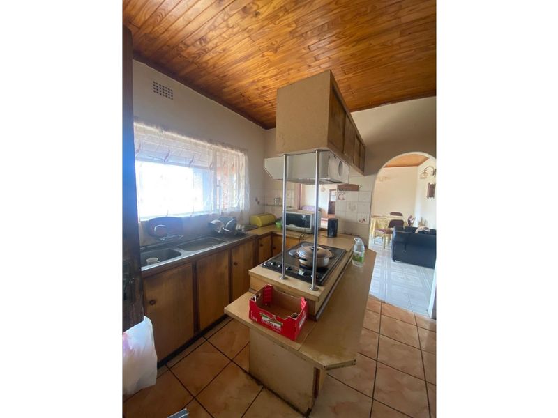A dated kitchen featuring wooden cabinetry, a central island with a built-in hob, and a distinctive timber-paneled ceiling.