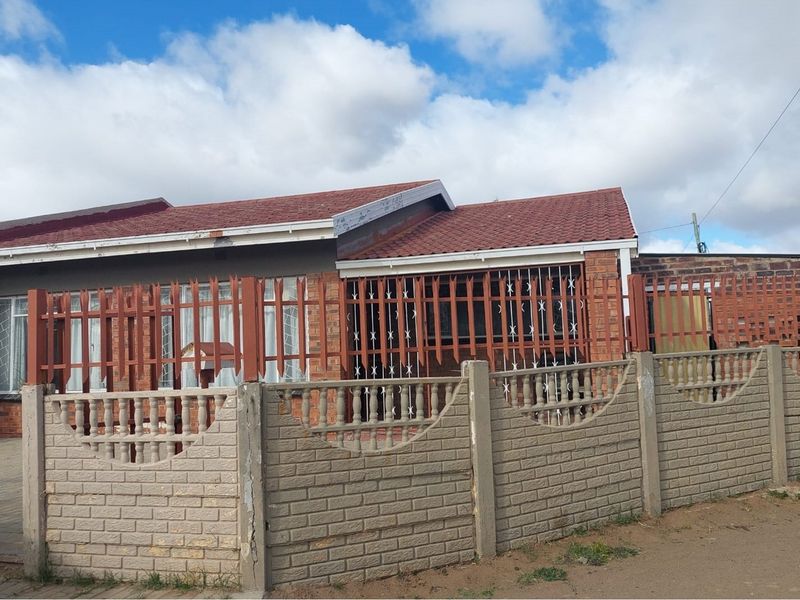 Front exterior view of a single-story brick house featuring a tiled roof, secure metal fencing, and a precast concrete boundary wall.