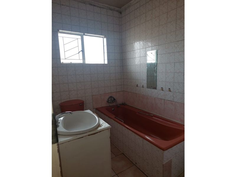 A dated bathroom featuring a colored bathtub, matching toilet, and a vanity basin with tiled walls and flooring.