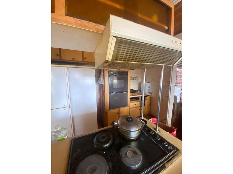 A dated kitchen featuring wooden cabinetry, a built-in oven, and a hob with an overhead extractor fan.