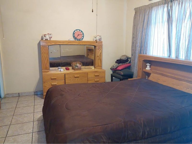 A bedroom featuring tiled flooring and a built-in headboard unit, offering a functional space with neutral wall finishes.