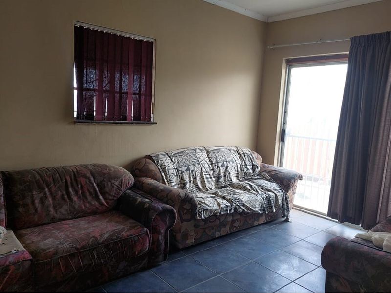 A living room featuring dark floor tiles, a sliding glass door leading to an outdoor area, and a window with vertical blinds.