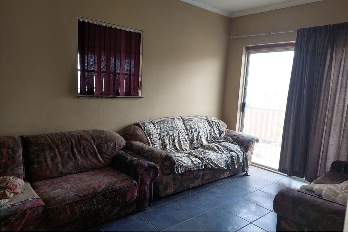 A living room featuring dark floor tiles, a sliding glass door leading to an outdoor area, and a window with vertical blinds.