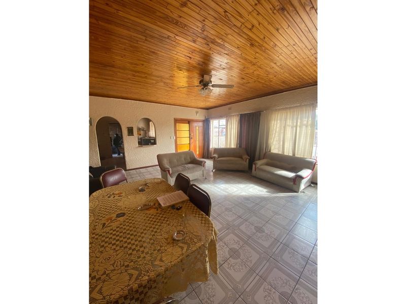 Spacious living and dining area featuring a high wood-paneled ceiling, tiled flooring, and arched wall openings leading to adjacent rooms.