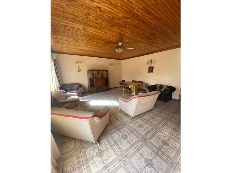 Spacious living and dining area featuring a distinctive timber-clad ceiling, tiled flooring, and wall-mounted lighting fixtures.