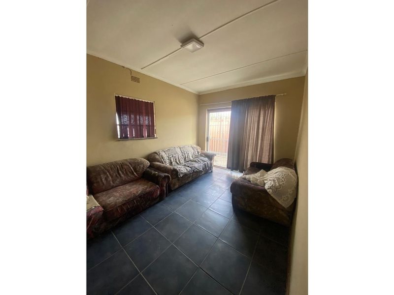 A living room featuring dark floor tiles, a sliding glass door leading to the exterior, and a small window with vertical blinds.