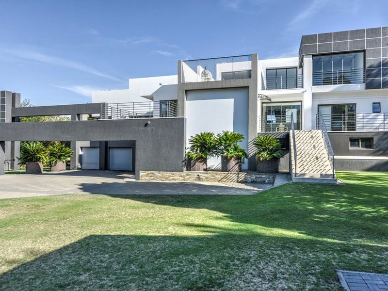 Modern multi-level residential facade featuring a double garage, paved driveway, upper-level balconies, and a well-maintained front lawn.