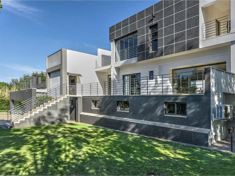 Rear view of a modern multi-level home featuring a raised terrace with stainless steel balustrades, external staircase, and contemporary tiled facade.