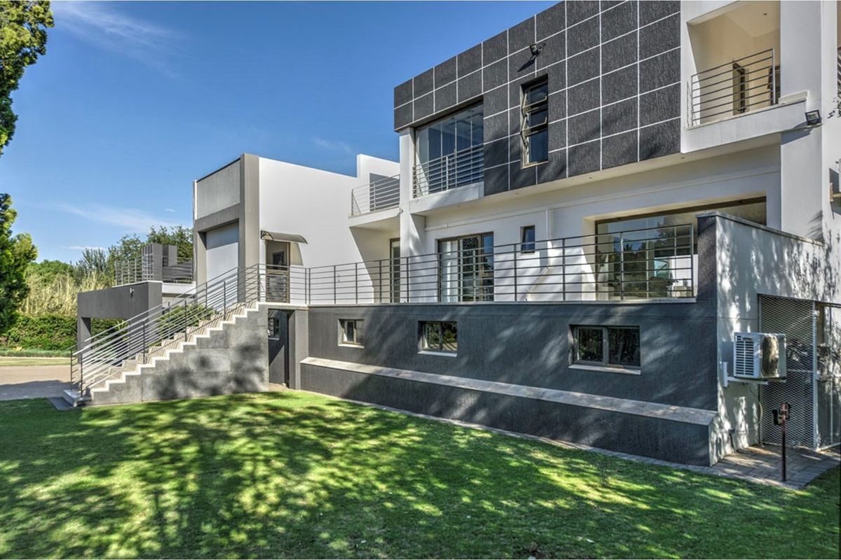 Rear view of a modern multi-level home featuring a raised terrace with stainless steel balustrades, external staircase, and contemporary tiled facade.