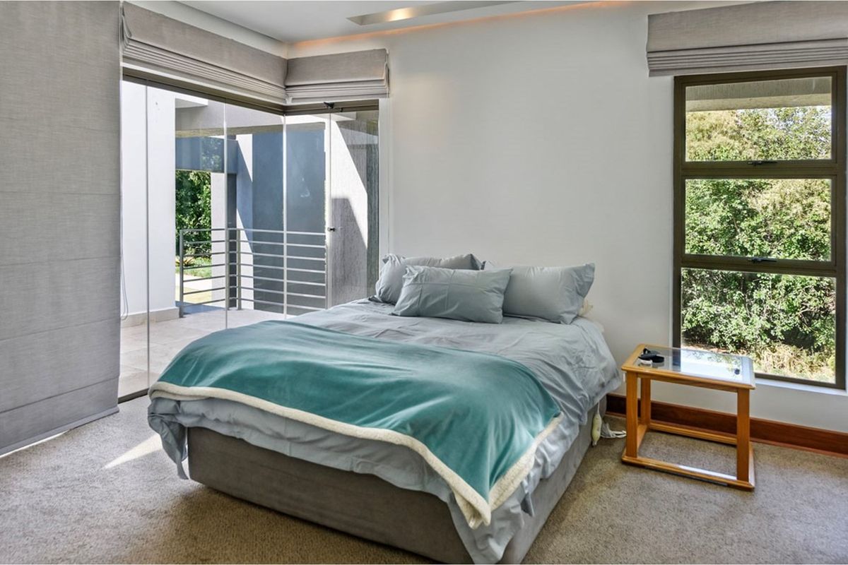A bright bedroom featuring large windows, sliding glass doors leading to an outdoor area, and recessed ceiling lighting.