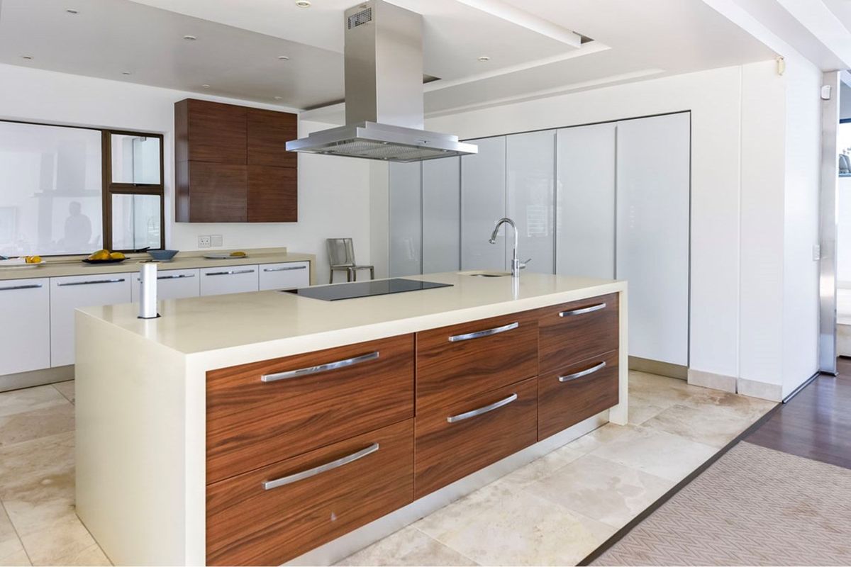 Modern kitchen featuring a large central island with stone countertops, wood veneer cabinetry, integrated induction hob, and high-end stainless steel extractor fan.