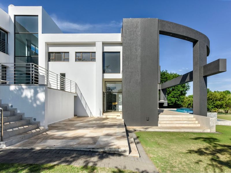 Modern rear elevation featuring a stone patio, architectural design elements, stainless steel railings, and a swimming pool set against a landscaped garden.