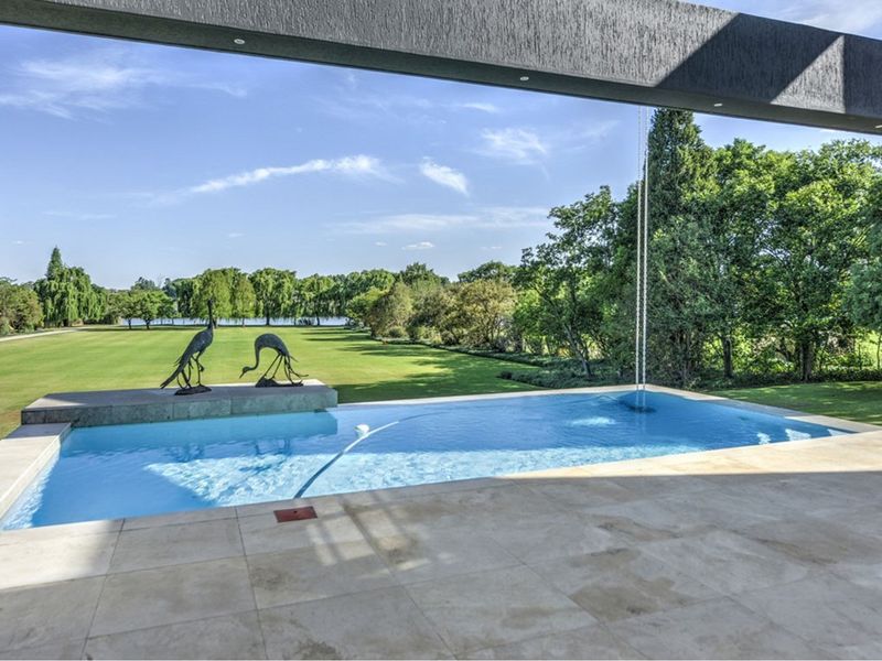 A modern covered patio overlooking a pristine swimming pool and expansive landscaped garden with scenic views.