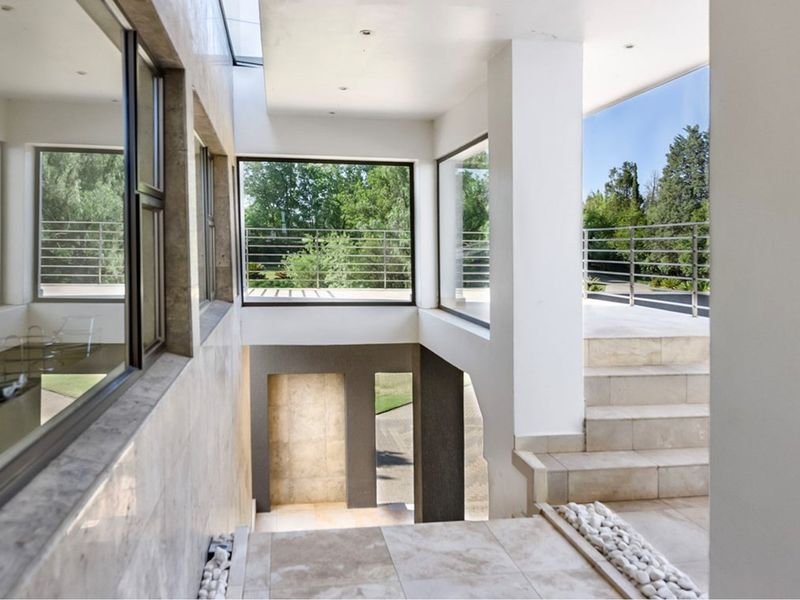 Modern architectural entrance hall featuring stone flooring, stone wall cladding, a striking staircase, and expansive windows providing natural light and garden views.