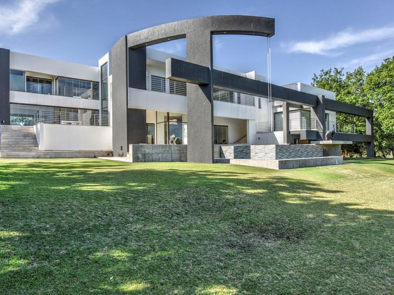 A striking modern architectural rear elevation featuring bold concrete structural elements, expansive glass sliding doors, and a well-maintained lawn.