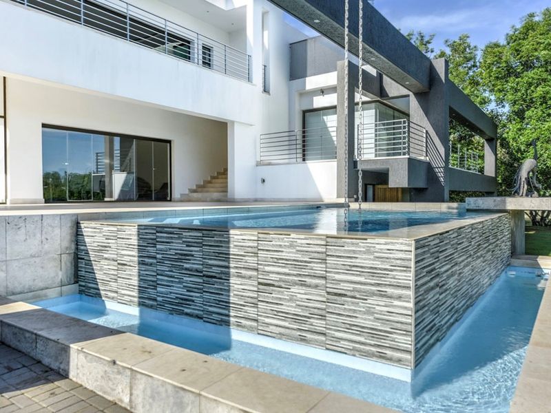 Modern architectural home featuring a raised swimming pool with stone cladding, water feature, and expansive outdoor patio area with balcony access.