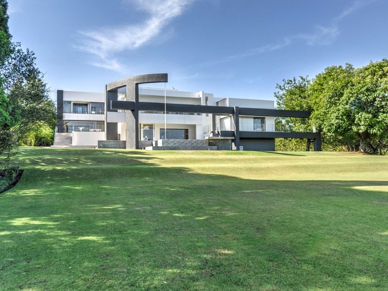 A striking modern architectural residence featuring bold structural elements, expansive balconies, and a well-maintained, spacious rear lawn.