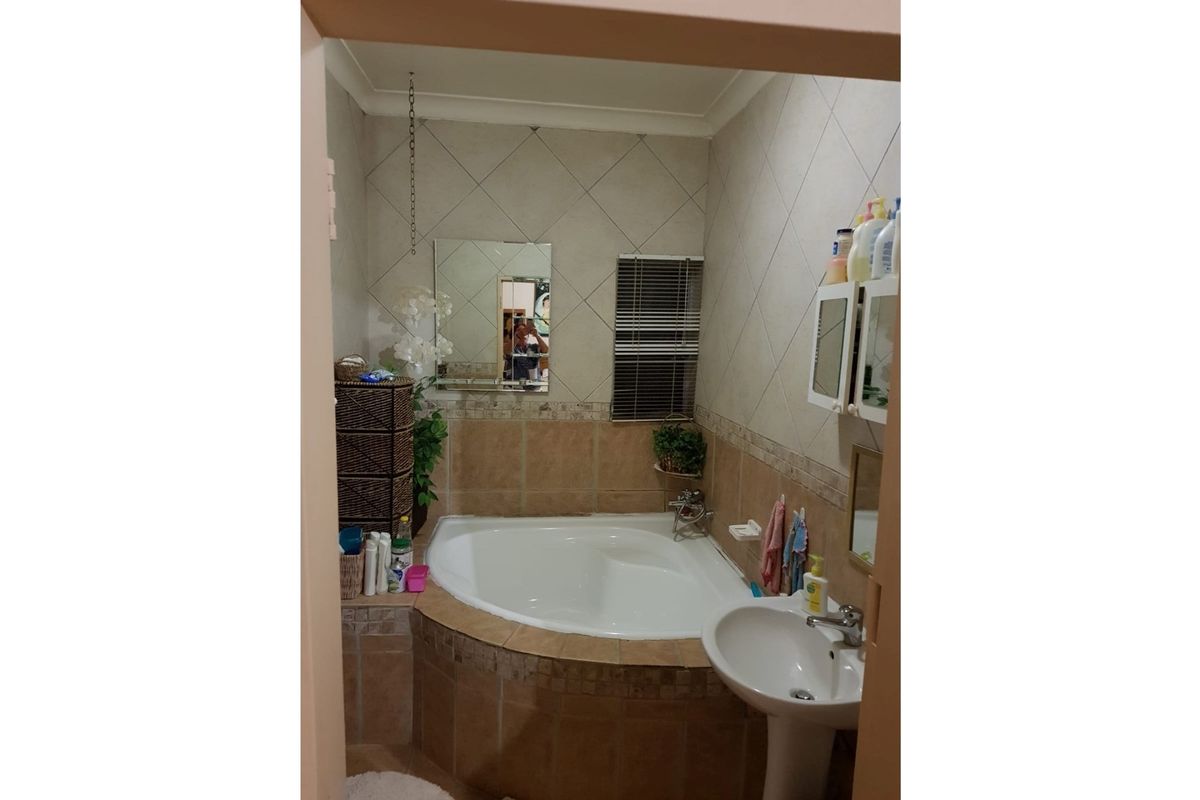 A compact bathroom featuring a corner bathtub with tiled surround and a pedestal basin, finished with neutral wall tiles.