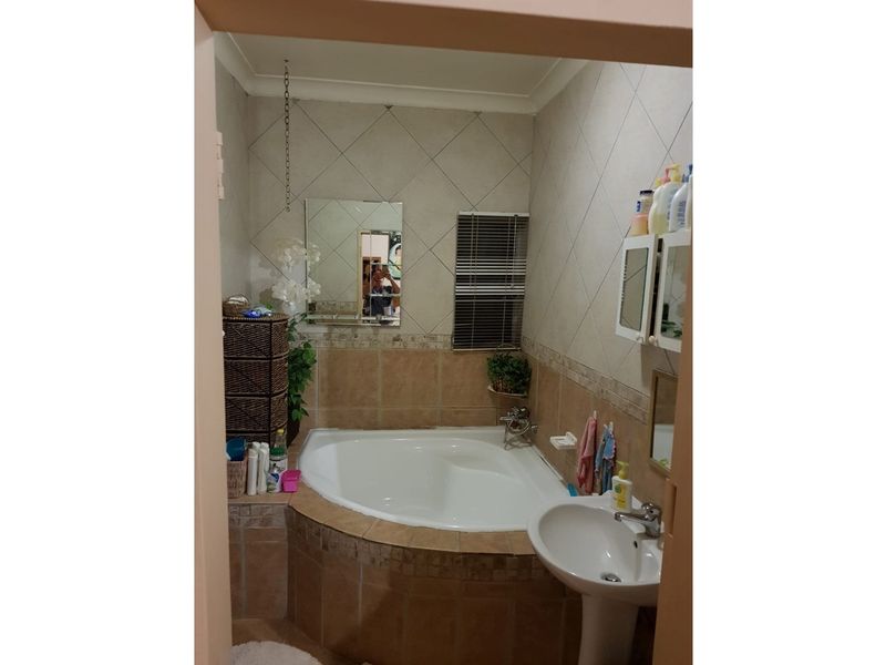 A compact bathroom featuring a corner bathtub with tiled surround and a pedestal basin, finished with neutral wall tiles.