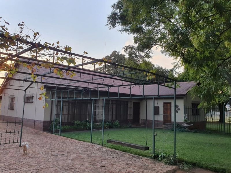 A view of the rear exterior of the farm property, featuring a paved driveway, a metal pergola structure, and a well-maintained lawn area.