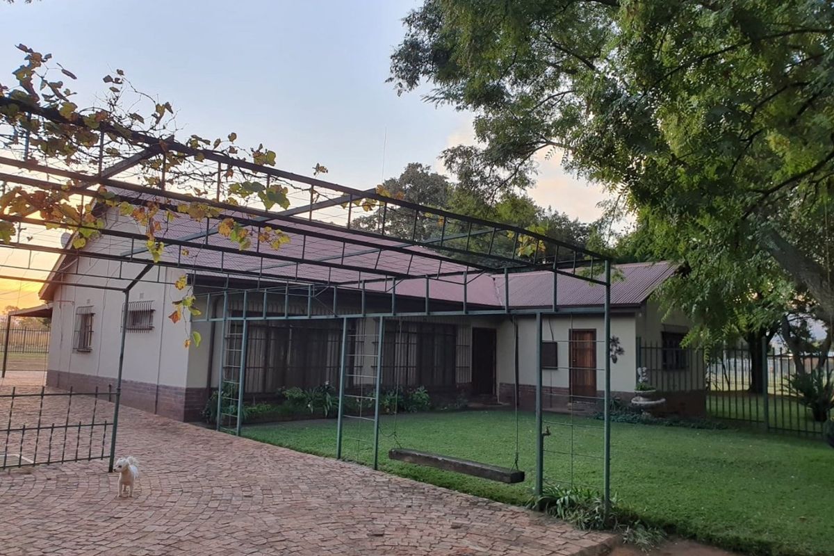 A view of the rear exterior of the farm property, featuring a paved driveway, a metal pergola structure, and a well-maintained lawn area.