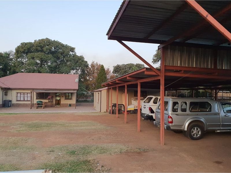 A farm property featuring a main dwelling with a tiled roof and an extensive open-sided metal carport structure for vehicle storage.