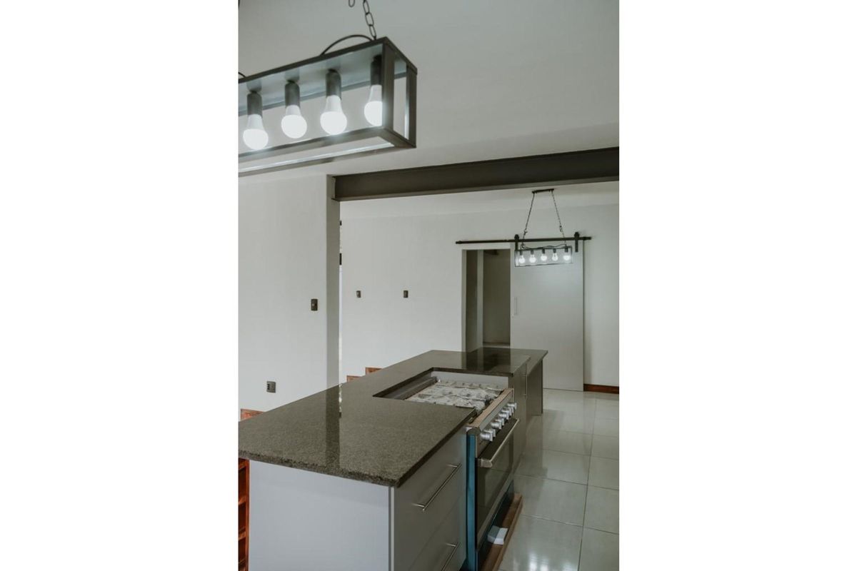 Modern kitchen featuring a central island with a built-in gas stove, granite countertops, and contemporary pendant lighting.