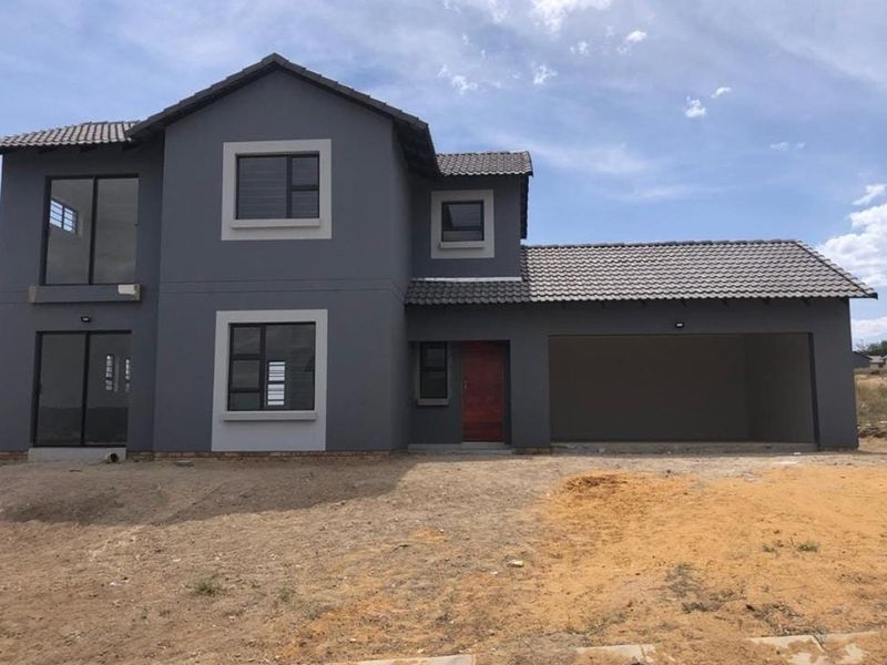A modern double-story house featuring a grey exterior, tiled roof, integrated garage, and large windows, set on an undeveloped plot.