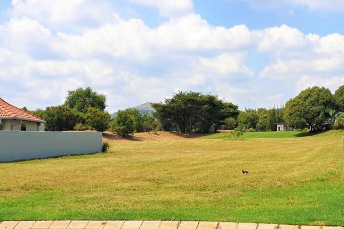 A spacious, well-maintained vacant residential plot featuring a level grassed area, boundary wall, and scenic landscape views.