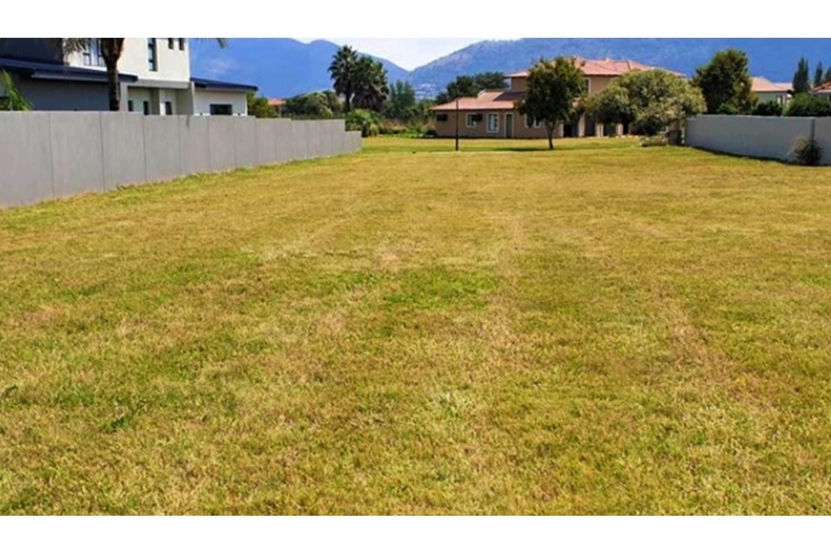 A level, vacant residential plot featuring established grass lawn and boundary walls, situated in a developed neighborhood with mountain views.