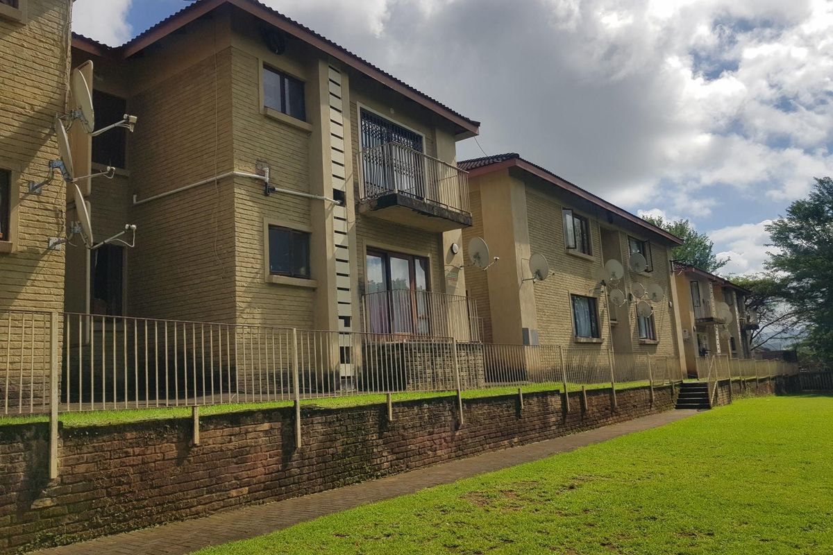 Exterior view of a multi-story apartment complex featuring brick facades, private balconies with metal railings, and a shared lawn area.
