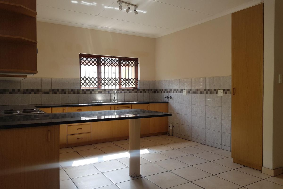 A functional kitchen featuring light wood cabinetry, granite countertops, tiled backsplash, and tiled flooring, with a built-in pantry and security-fitted window.