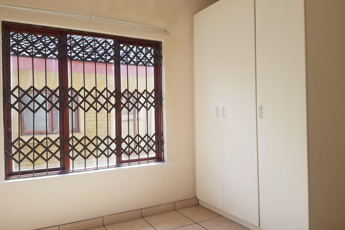 A vacant bedroom featuring built-in cupboards, tiled flooring, and a window fitted with a security gate.