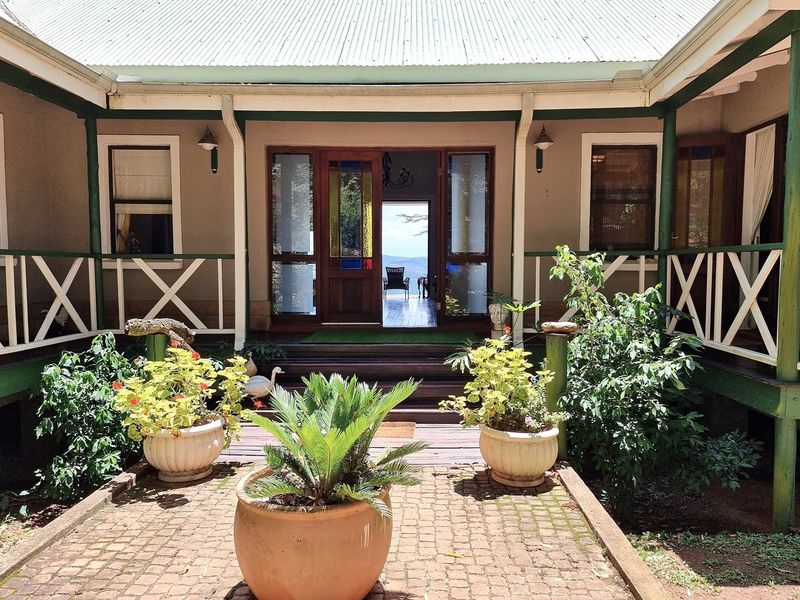 A charming rear courtyard featuring timber decking, a covered veranda with balustrades, and a central entrance leading into the home with a view beyond.