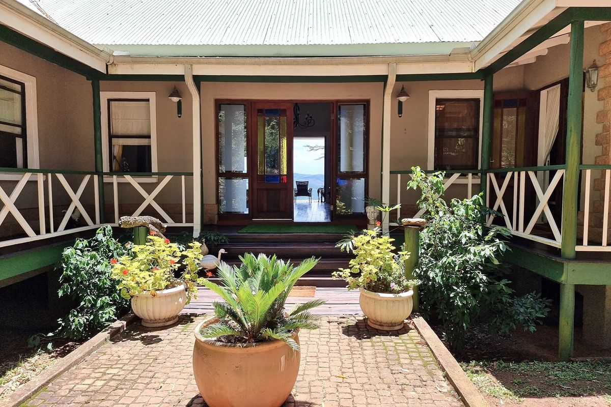 A charming rear courtyard featuring timber decking, a covered veranda with balustrades, and a central entrance leading into the home with a view beyond.