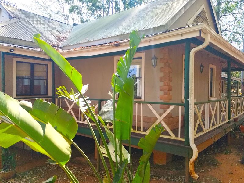 A rear view of a cottage-style house featuring a wrap-around veranda, corrugated metal roofing, and decorative brick corner detailing.
