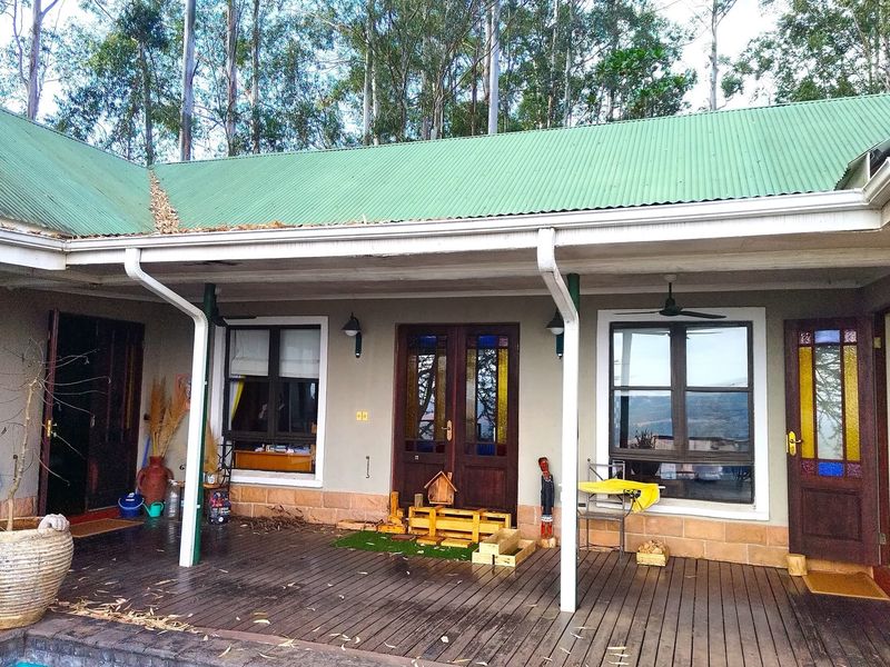 A covered timber deck patio featuring stone cladding, stained glass timber doors, and ceiling fans, overlooking the garden area.