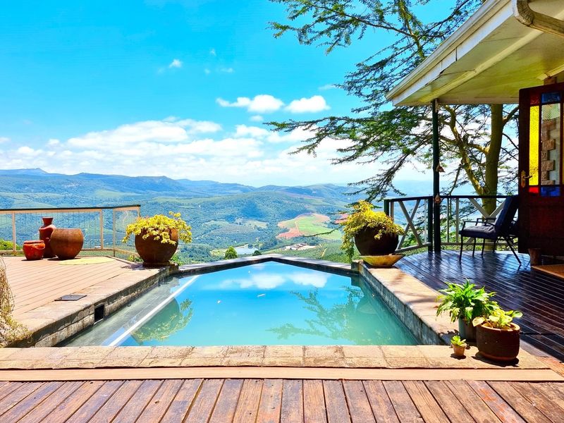 A scenic outdoor pool area featuring timber decking and a covered patio, offering expansive mountain and landscape views.