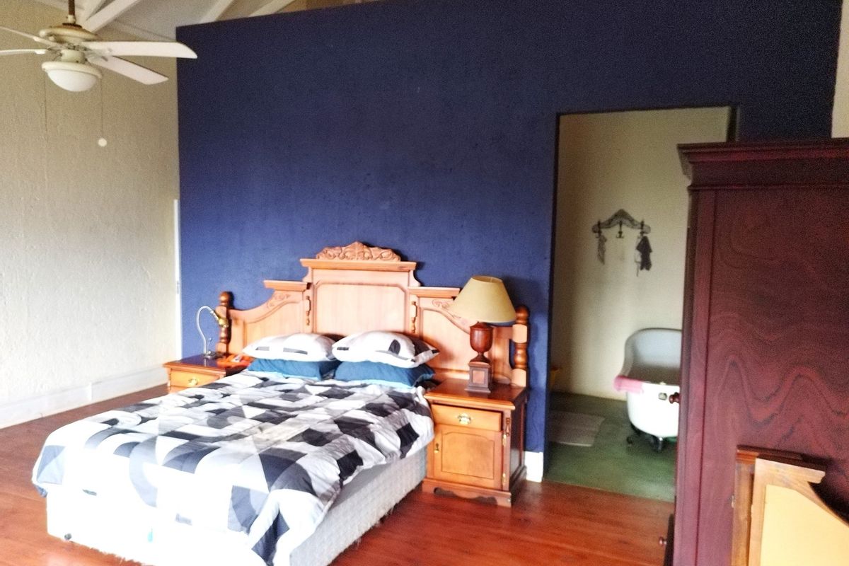 Spacious bedroom featuring timber flooring, exposed rafters, and a ceiling fan, with an adjoining en-suite bathroom area.