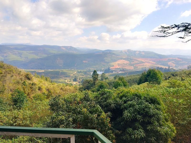 A scenic elevated view overlooking lush green hills, valleys, and distant mountains, captured from a balcony with a metal railing.