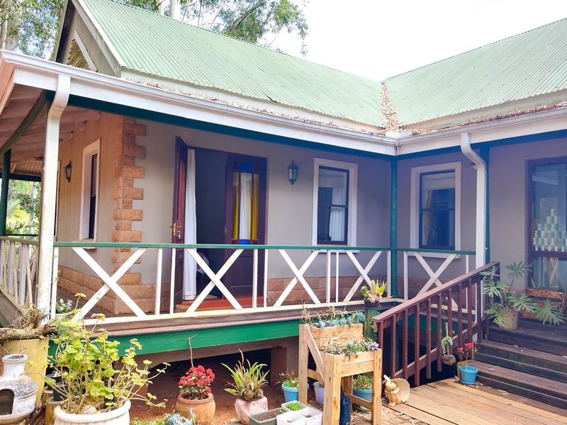 A rear view of the house featuring a wrap-around timber deck, stairs, and a corrugated metal roof with stone corner detailing.