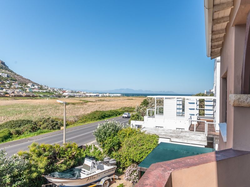 Elevated view from a balcony overlooking a coastal road, surrounding landscape, and distant mountain range.