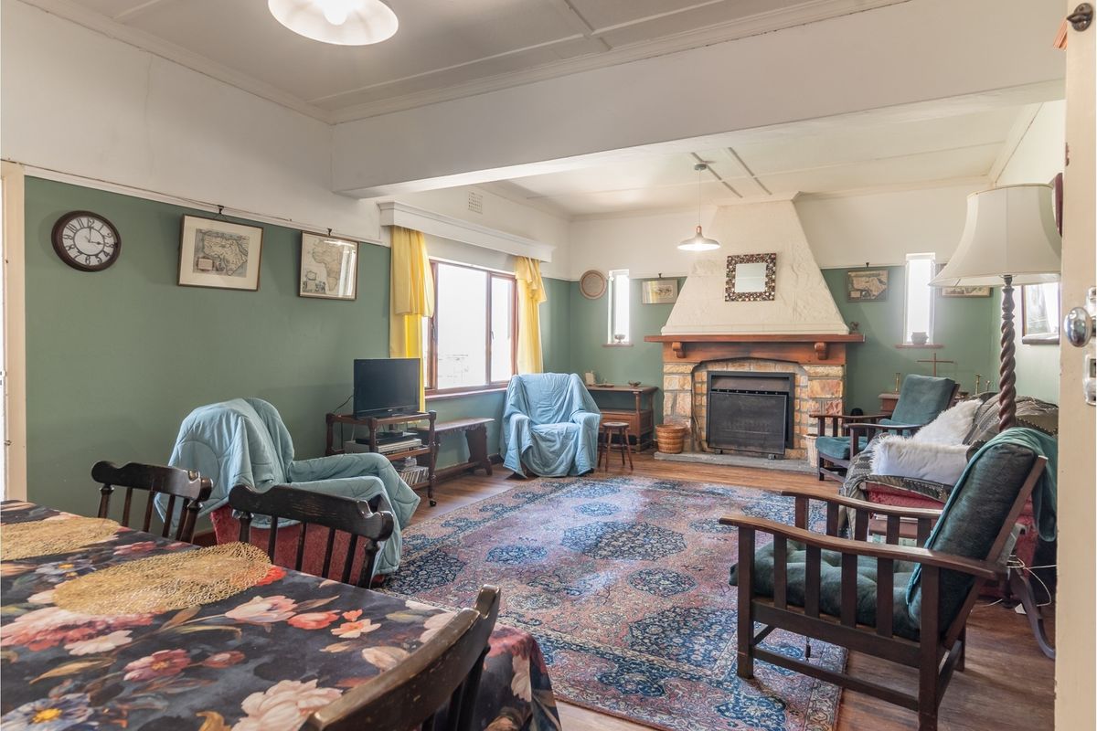 Spacious living room featuring a prominent stone fireplace, timber flooring, and classic picture rails, offering a warm and traditional atmosphere.
