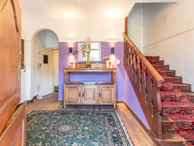 Welcoming entrance hall featuring a classic timber staircase with balustrade, hardwood flooring, and an elegant arched doorway leading to adjacent living spaces.