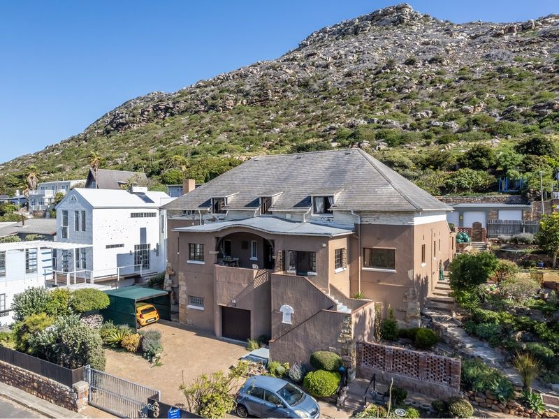 Aerial view of a multi-level residential property featuring a tiled roof, covered balcony, and stone masonry, set against a mountain backdrop.