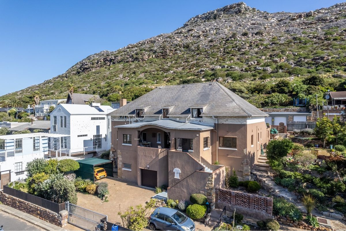 Aerial view of a multi-level residential property featuring a tiled roof, covered balcony, and stone masonry, set against a mountain backdrop.